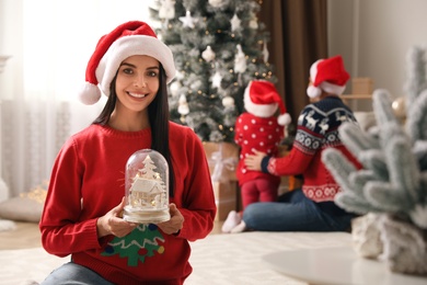 Woman in red Christmas sweater holding decorative snow globe at home