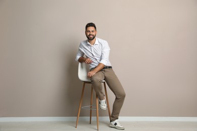 Handsome young man sitting on stool near beige wall