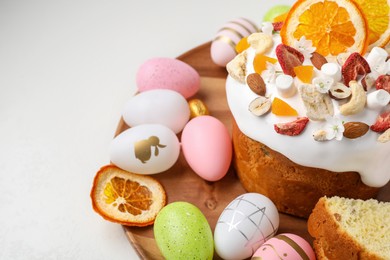 Photo of Traditional Easter cake with dried fruits and painted eggs on white table, closeup. Space for text