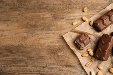 Chocolate bars with nuts and parchment on wooden table, flat lay. Space for text