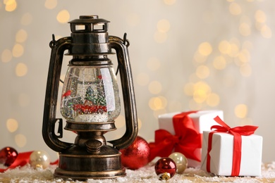 Beautiful snow globe in vintage lantern, gift boxes and Christmas decor on table against blurred festive lights