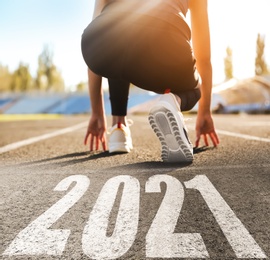 Start new year with fresh vision and ideas. Sporty woman ready for running near 2021 numbers on road, closeup