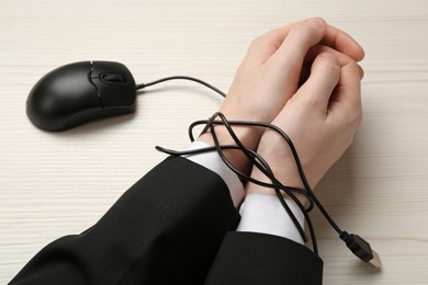 Photo of Man showing hands tied with computer mouse cable at white wooden table, closeup. Internet addiction