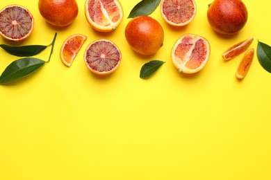 Many ripe sicilian oranges and leaves on yellow background, flat lay. Space for text