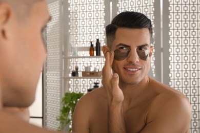 Man applying dark under eye patch near mirror at home
