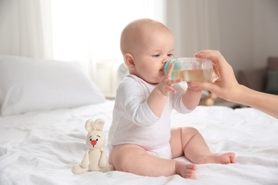 Lovely mother giving her baby drink from bottle on bed in room