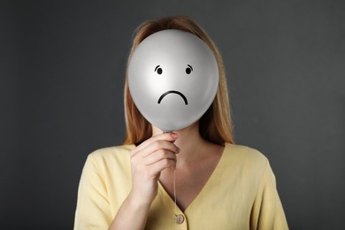 Woman hiding behind balloon with sad face on grey background. Depression concept