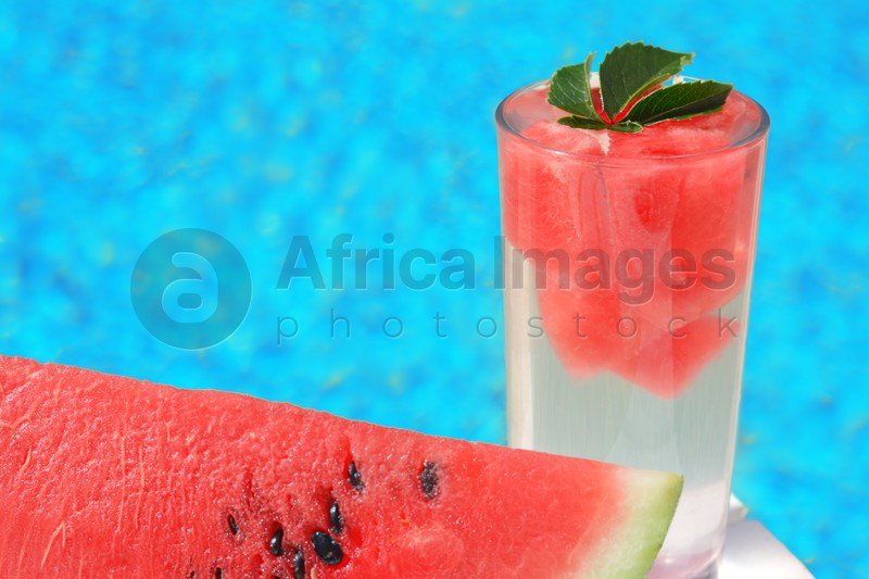 Refreshing drink in glass and sliced watermelon near swimming pool outdoors, closeup