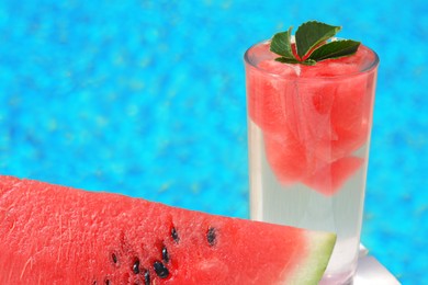 Refreshing drink in glass and sliced watermelon near swimming pool outdoors, closeup