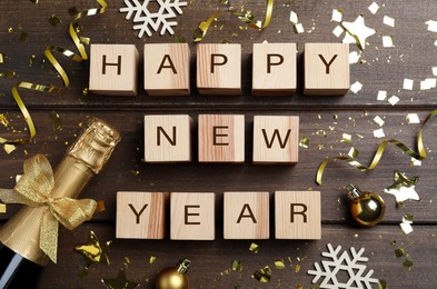 Phrase Happy New Year made of cubes, sparkling wine and festive decor on wooden background, flat lay
