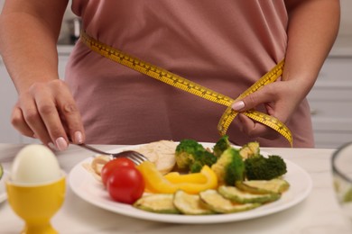 Overweight woman measuring waist while having meal at home, closeup 