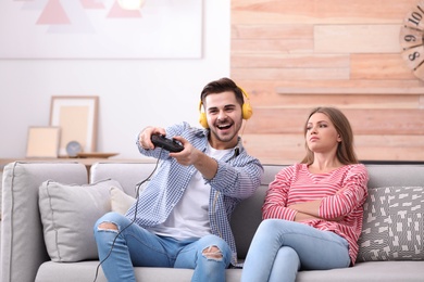 Displeased woman sitting near her man playing video games at home