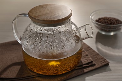 Photo of Glass teapot with aromatic buckwheat tea and granules on wooden table, closeup