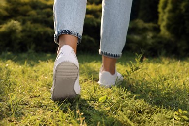 Photo of Woman in jeans and white shoes walking on green grass, closeup