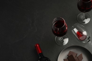 Composition with tasty red wine and chocolate on black table, above view. Space for text