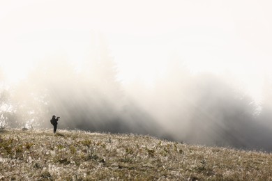 Photo of Photographer near foggy forest lit by morning sun. Beautiful landscape
