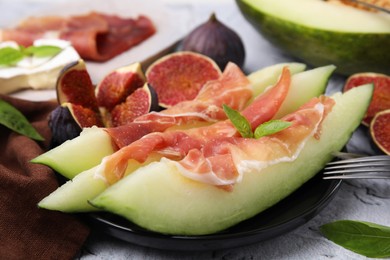 Tasty melon, jamon and figs served on white textured table, closeup