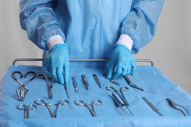 Doctor taking surgical instruments from table on light background, closeup