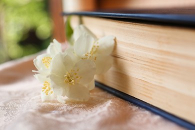 Photo of Beautiful jasmine flowers near book on pink fabric, closeup