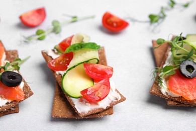 Tasty rye crispbreads with salmon, cream cheese and vegetables on light grey table, closeup