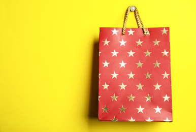 Red shopping paper bag with star pattern on yellow background, space for text