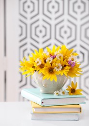 Photo of Beautiful bright flowers in cup and books on white table indoors