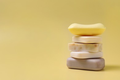 Photo of Many different soap bars stacked on yellow background, space for text