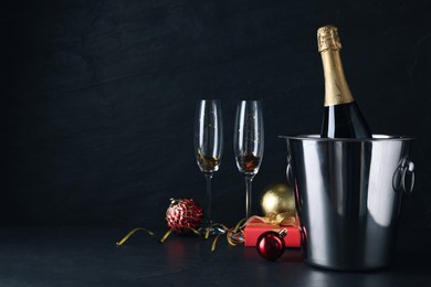 Happy New Year! Bottle of sparkling wine in bucket and glasses on black background