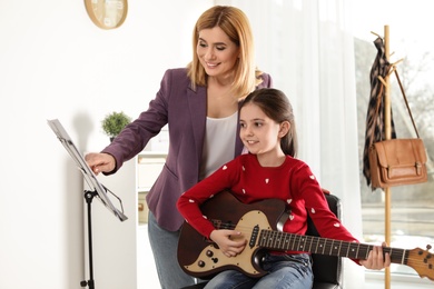 Little girl playing guitar with her teacher at music lesson. Learning notes