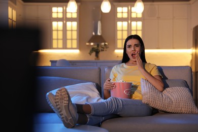 Young woman watching movie with popcorn on sofa at night, space for text