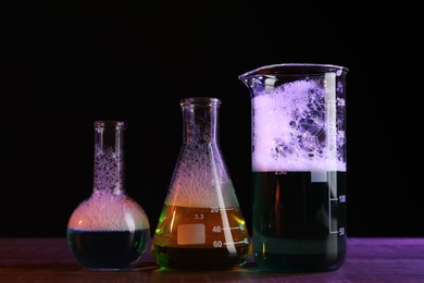 Photo of Laboratory glassware with colorful liquids on wooden table against black background. Chemical reaction