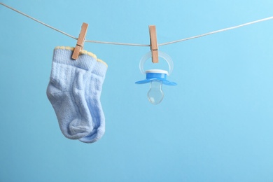 Small socks and pacifier hanging on washing line against color background, space for text. Baby accessories