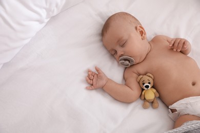Adorable baby with pacifier and toy bear sleeping on bed, top view. Space for text