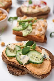 Delicious sandwiches with hummus and ingredients on white table