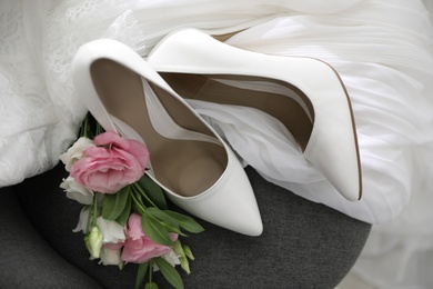 Pair of white high heel shoes, flowers and wedding dress on chair