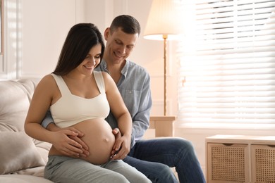 Man touching his pregnant wife's belly at home. Space for text