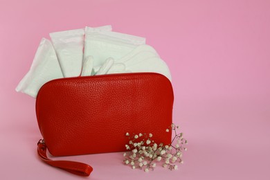 Menstrual pads, pantyliners and tampons in bag near flowers on pink background