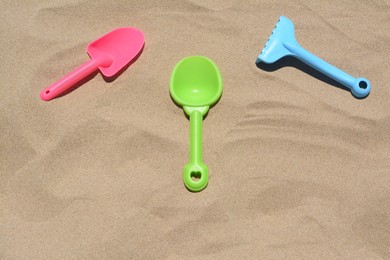 Photo of Bright plastic rake and shovels on sand, above view. Beach toys
