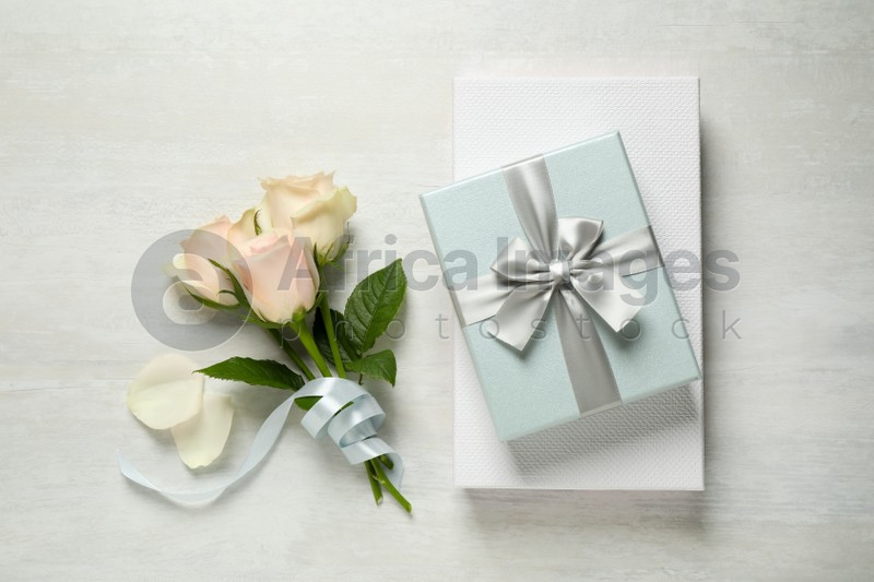 Elegant gift boxes and beautiful flowers on white table, flat lay