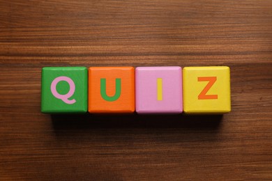 Colorful cubes with word Quiz on wooden table, flat lay