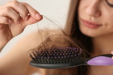 Photo of Woman untangling her hair from brush on light background, closeup