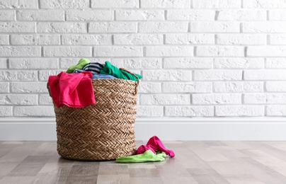Wicker basket with dirty laundry on floor near white brick wall