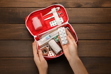Woman taking pills from first aid kit at wooden table, top view
