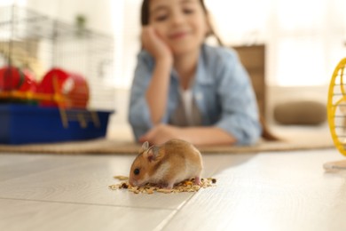 Photo of Little girl feeding her hamster at home, focus on pet