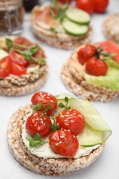 Crunchy buckwheat cakes with cream cheese, tomatoes and cucumber slices on white table, closeup