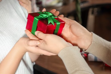 Photo of Young woman giving gift to her friend in cafe, closeup