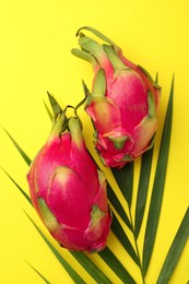 Delicious pitahaya fruits with palm leaf on yellow background, flat lay