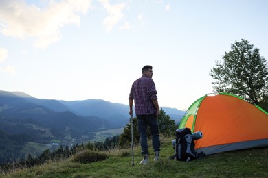 Tourist with backpack and sleeping pad near camping tent in mountains