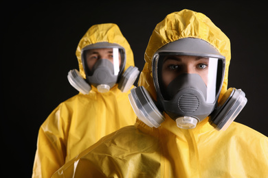 Man and woman wearing chemical protective suits on black background. Virus research