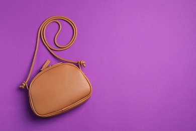 Photo of Stylish leather handbag on purple background, top view. Space for text
